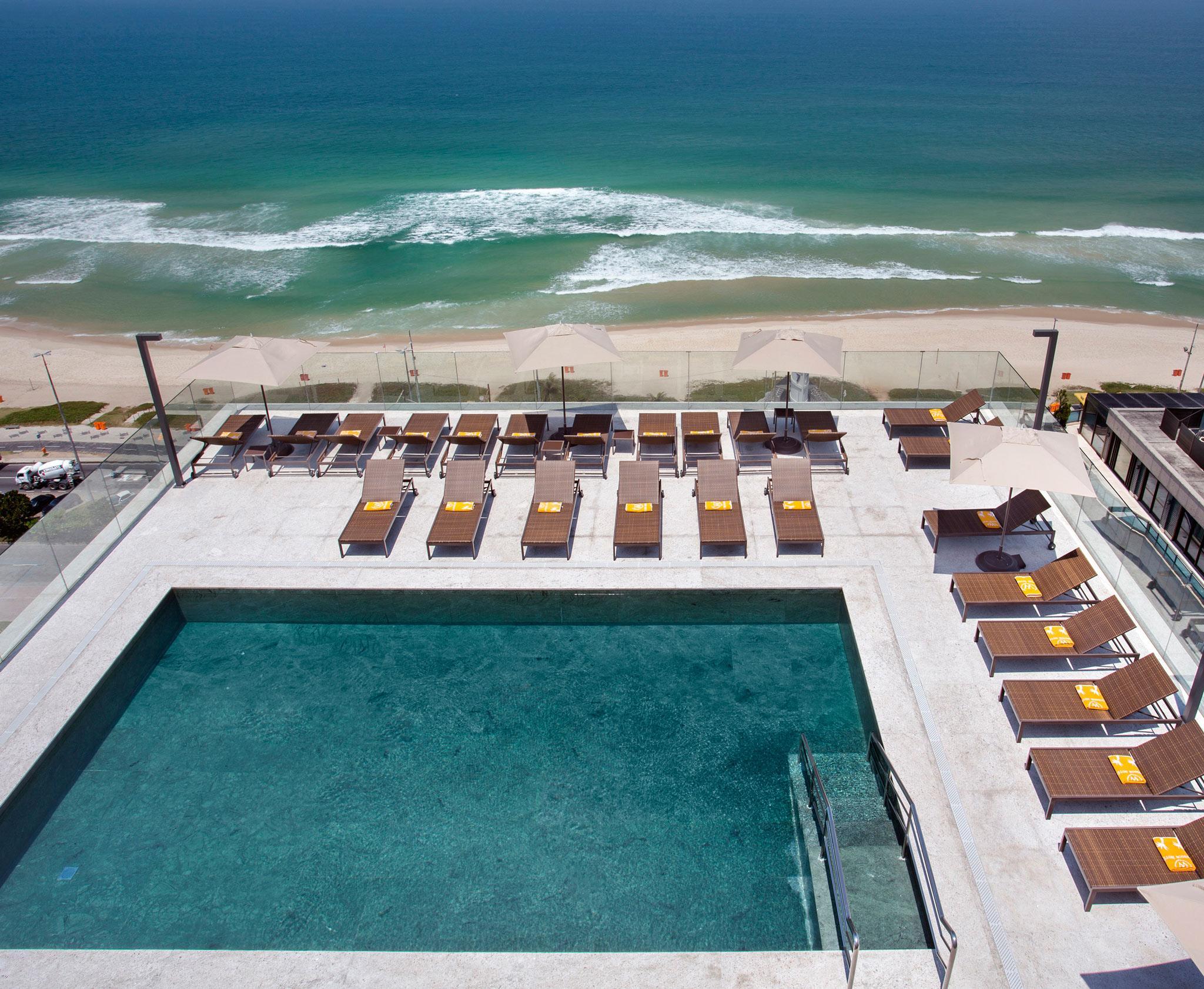 Windsor Marapendi Hotel Rio de Janeiro Bagian luar foto The photo shows a rooftop area with a swimming pool and several lounge chairs arranged around it. The pool has a clear blue surface, and the lounge chairs are positioned in a neat row, some with yellow cushions. In the background, you can see a beaut