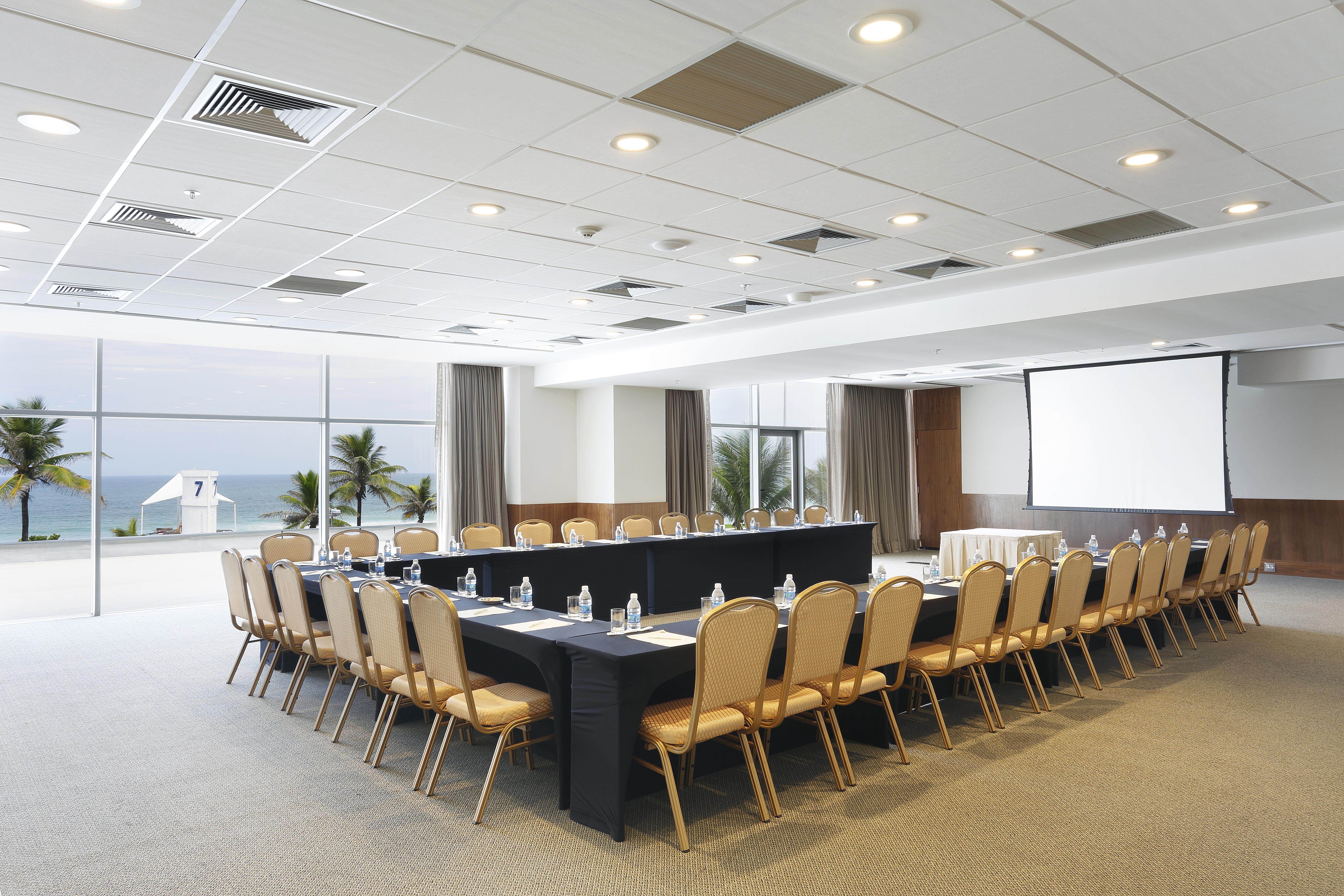 Windsor Marapendi Hotel Rio de Janeiro Bagian luar foto The photo shows a spacious conference room set up for a meeting. It features a long, rectangular table surrounded by a number of beige chairs. At the front, there is a large screen, likely for presentations. The room has large windows that provide a 
