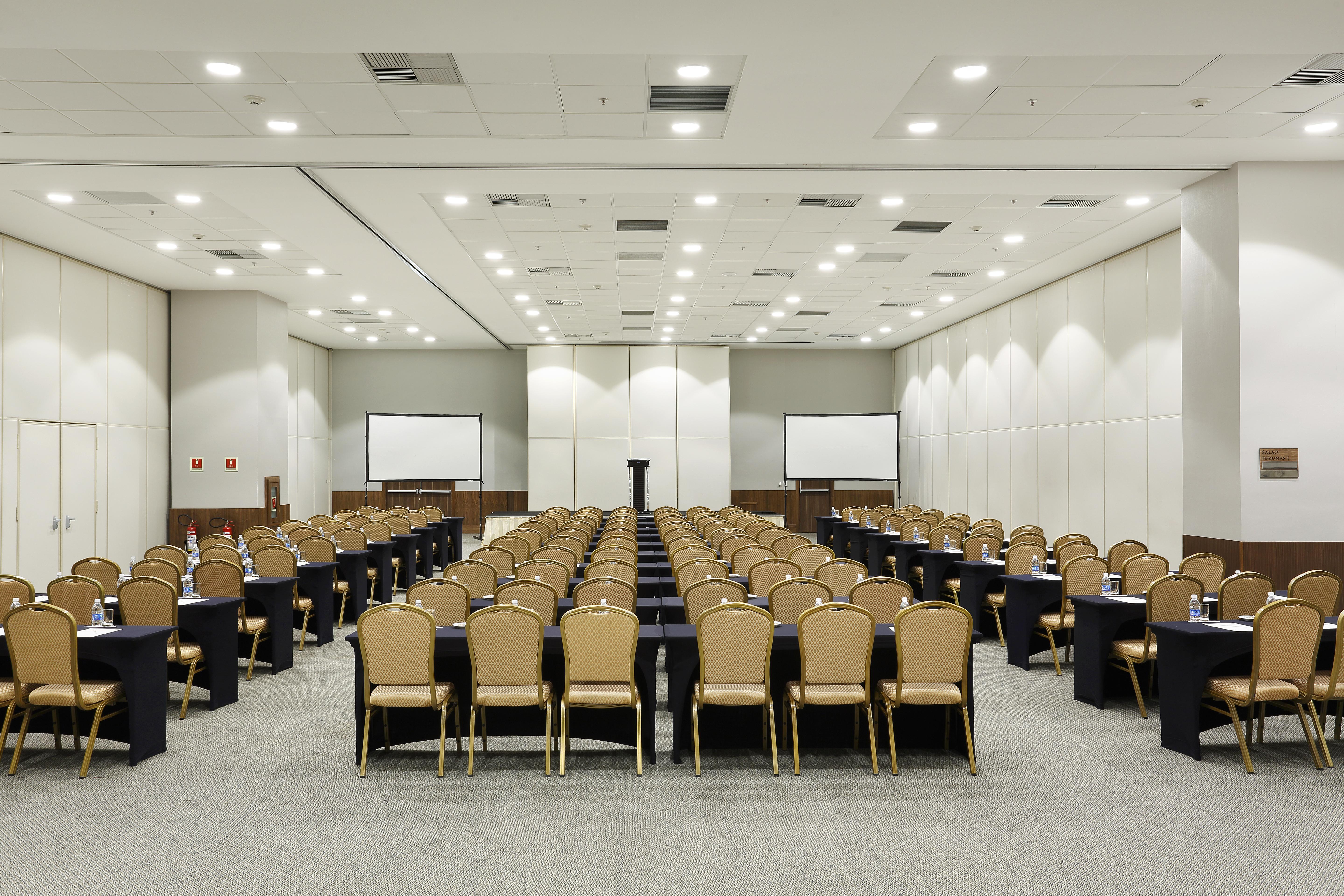 Windsor Marapendi Hotel Rio de Janeiro Bagian luar foto The photo shows a conference room arranged for an event or meeting. There are rows of neatly arranged chairs with golden frames, paired with black tables. The room has bright overhead lighting and features two blank screens in the front, likely for p