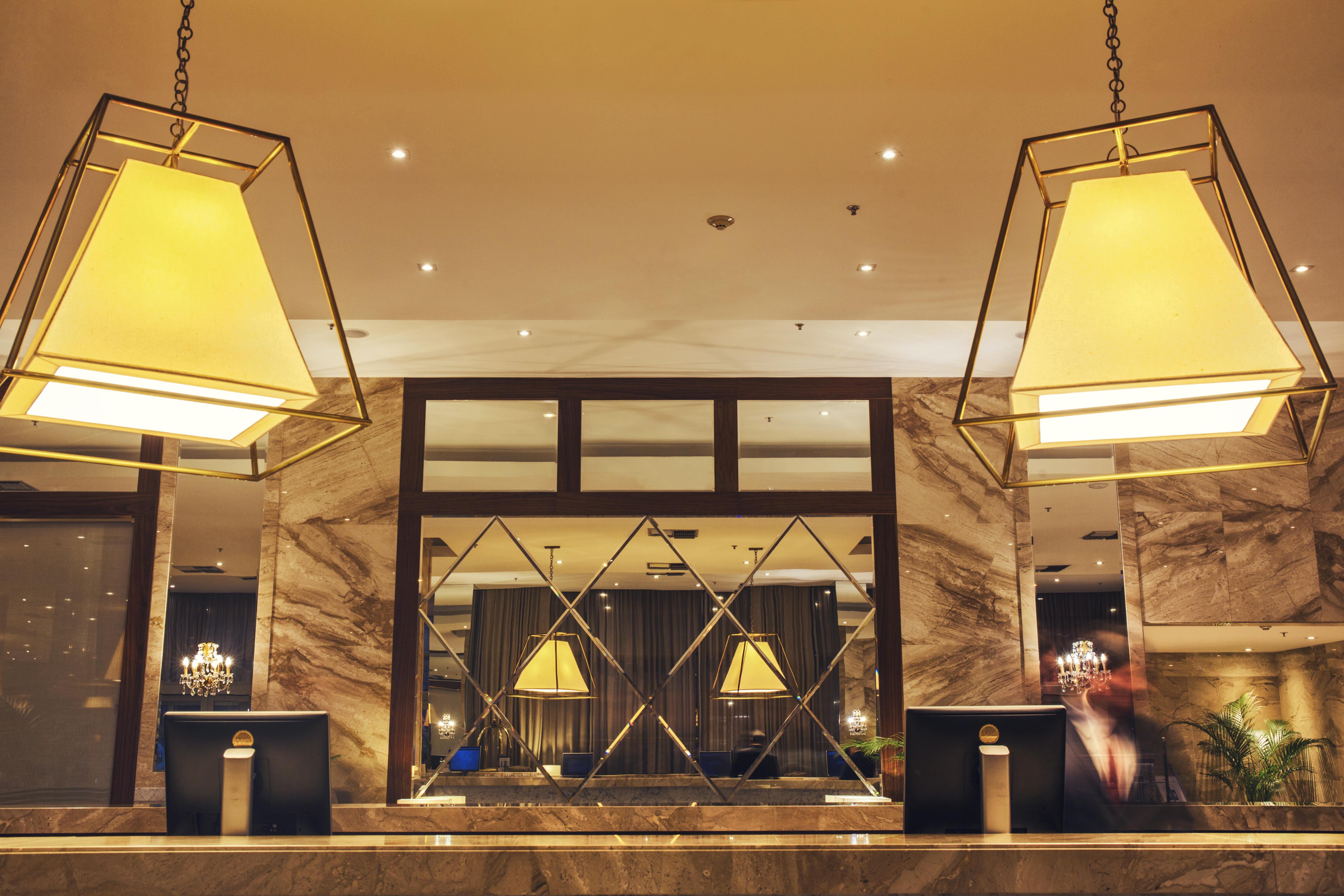 Windsor Marapendi Hotel Rio de Janeiro Bagian luar foto The photo shows a hotel lobby or reception area. There are large geometric light fixtures hanging from the ceiling, providing a warm glow to the space. The reception desk is made of a polished material, likely marble, with decorative elements and two